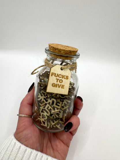 The Swear Jar of letters and cork lid held by a hand, the perfect gift of Fucks to Give.