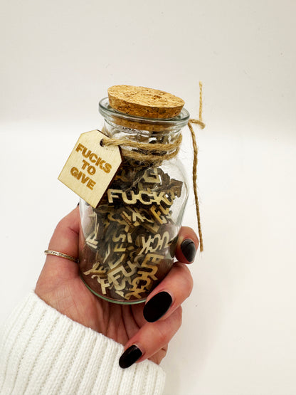 Hand holding The Swear Jar with cork and a tag labeled 'Fucks to Give'.